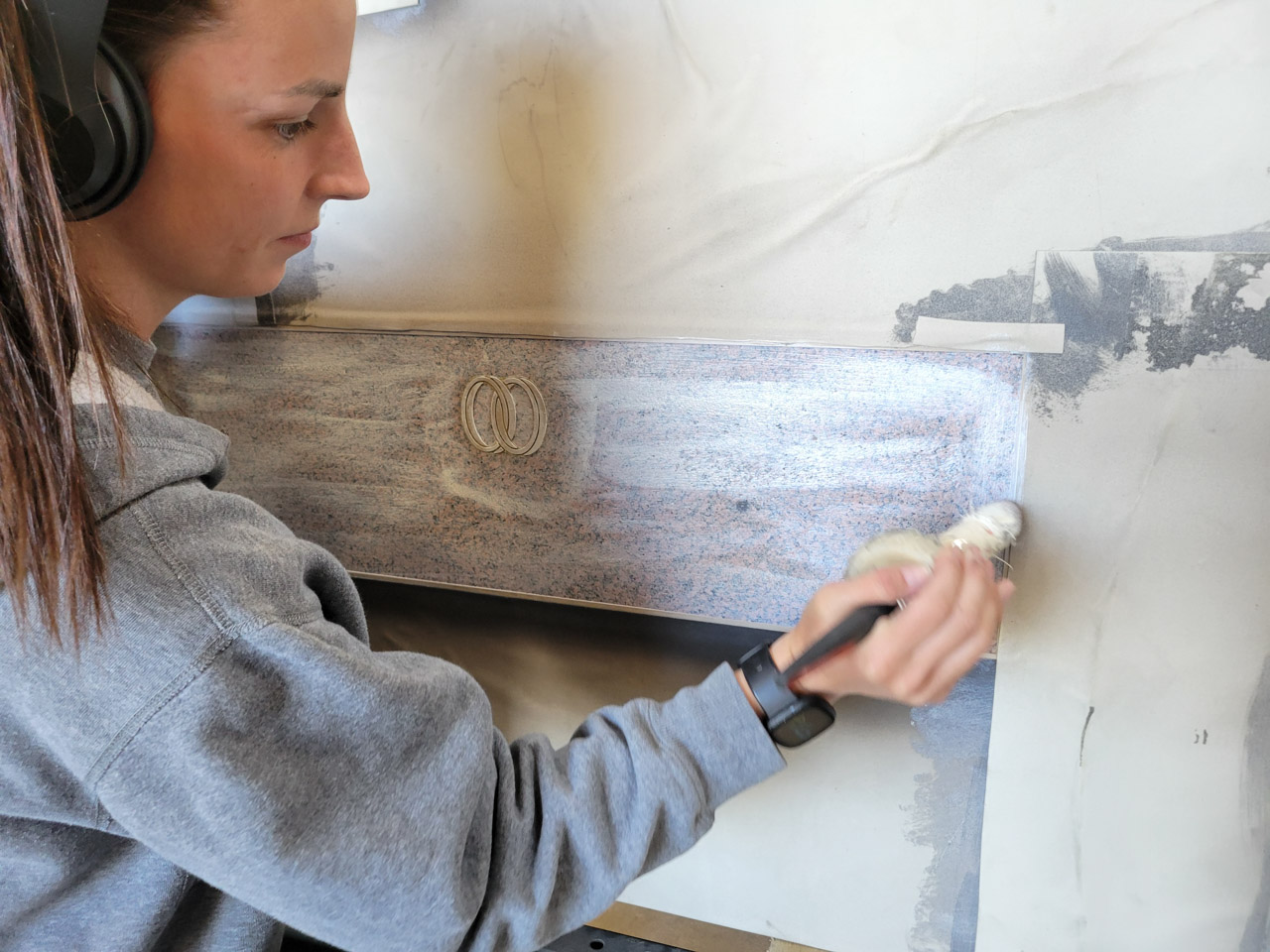 Professional artist carefully applying a stencil to a grey granite monument in preparation for sandblasting