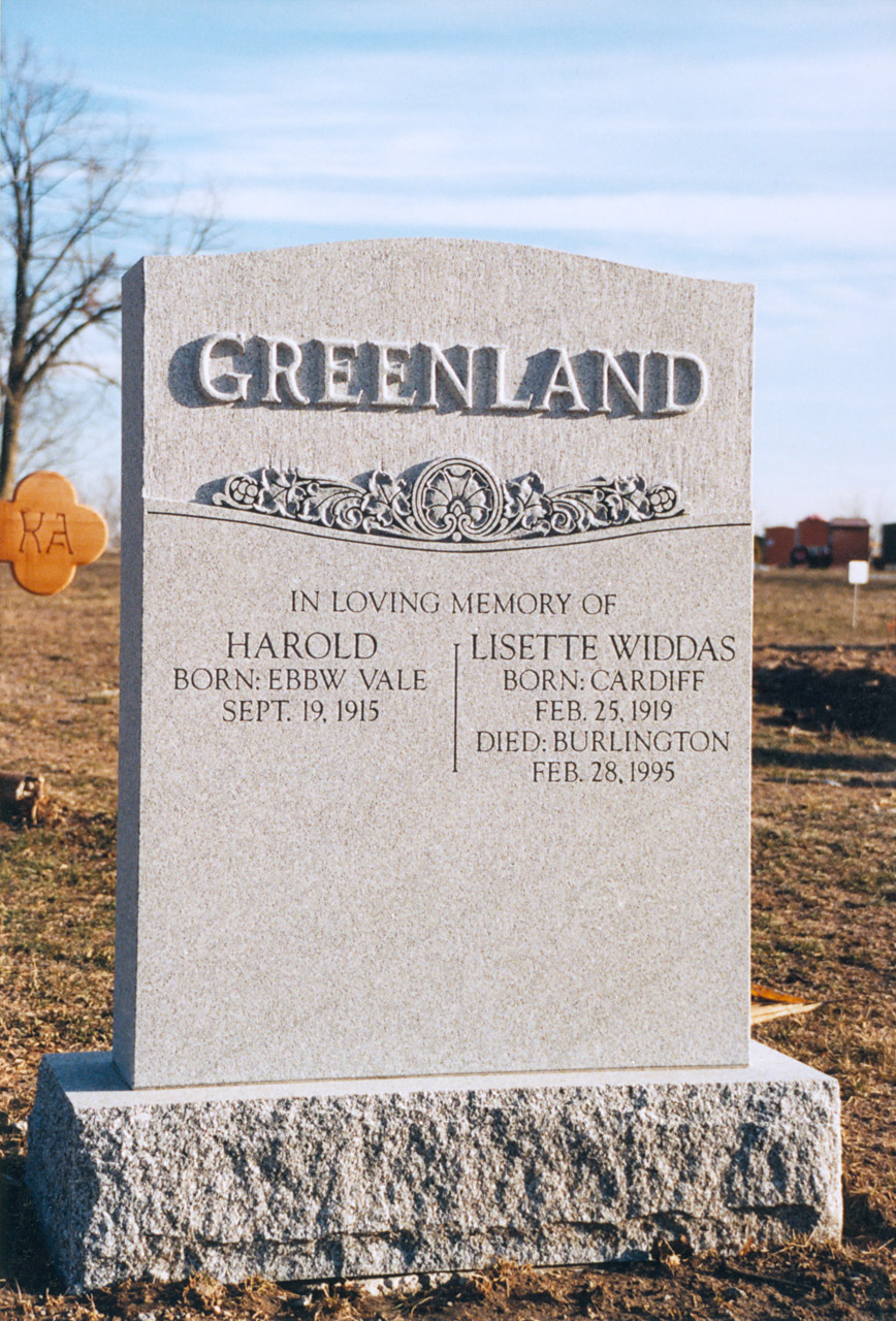 Grey granite headstone placed in an open public setting.