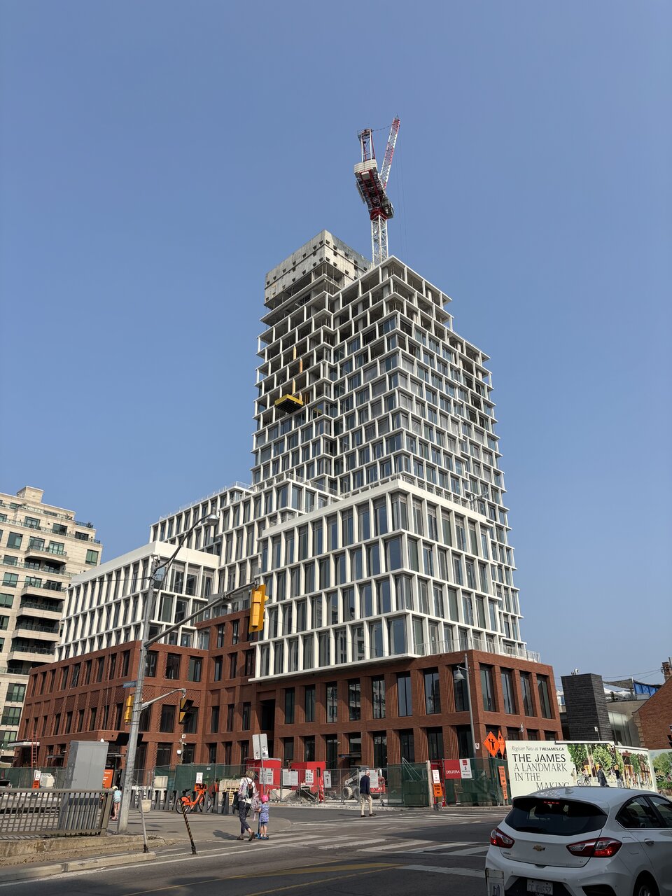 A modern multi-story building under construction rises above a city intersection on a clear day.