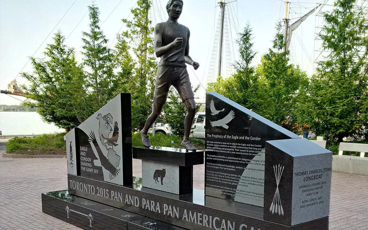 Bronze athlete statue rises above plaques forming a calm outdoor memorial among trees.